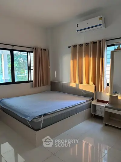 Spacious bedroom with large windows and modern furnishings, featuring an air conditioner for comfort.