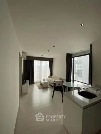 Modern living room with open kitchen, featuring sleek design and large windows for natural light.