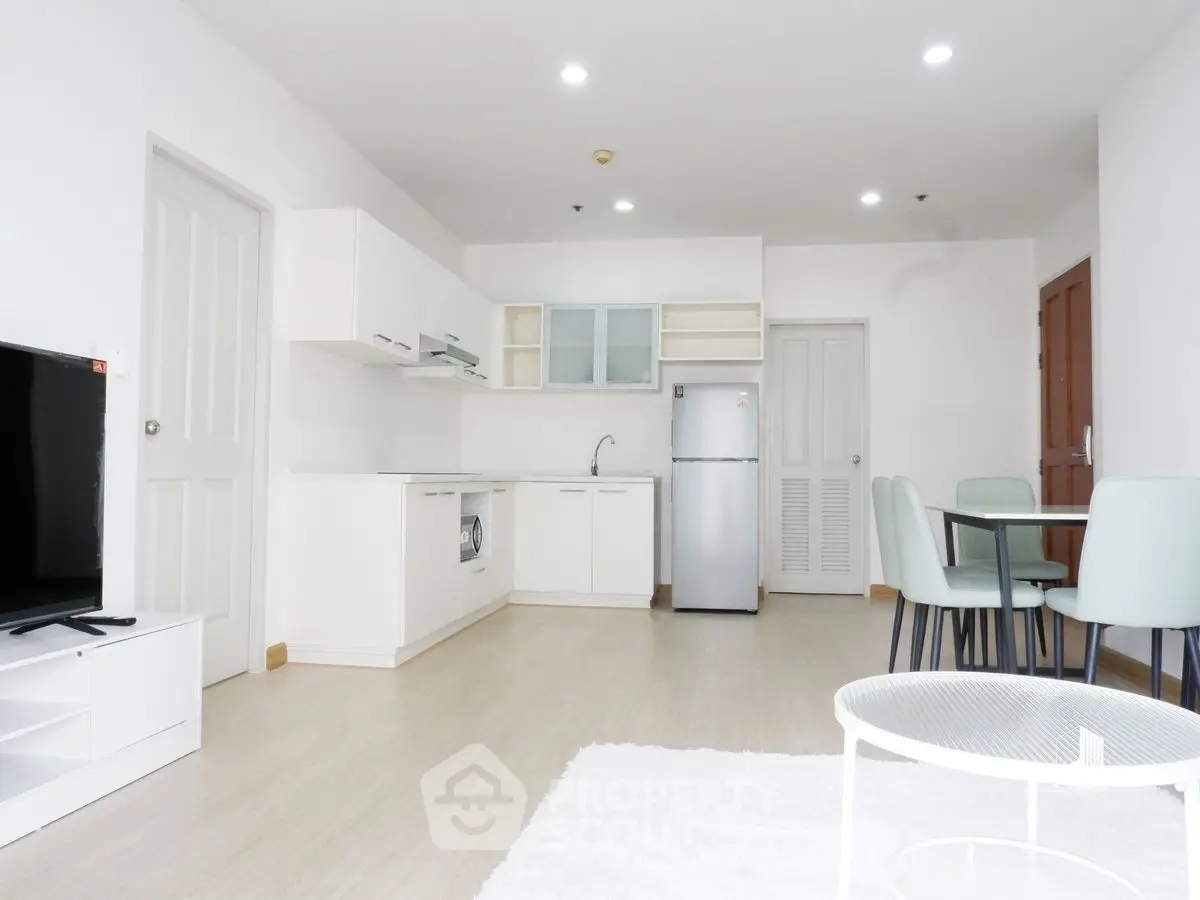 Modern open-plan living room with kitchen and dining area, featuring sleek white furniture and appliances.