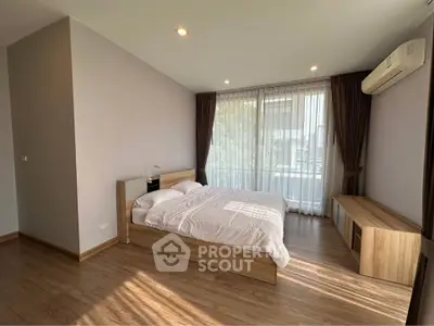 Spacious bedroom with modern wooden flooring and large windows for natural light.