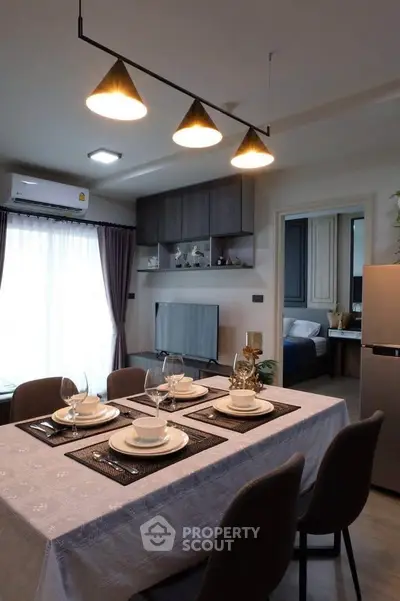 Modern dining area with elegant table setting and view into cozy bedroom, featuring stylish lighting and contemporary decor.