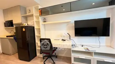 Modern studio apartment with sleek kitchen and workspace, featuring a black fridge and wall-mounted TV.