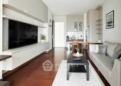 Modern living room with sleek furniture and open kitchen layout, featuring a large TV and stylish decor.