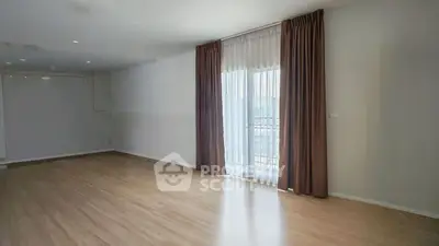Spacious empty living room with wooden flooring and large window with curtains.