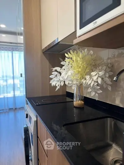 Modern kitchen with sleek black countertop and built-in appliances, featuring a stylish vase with decorative foliage.