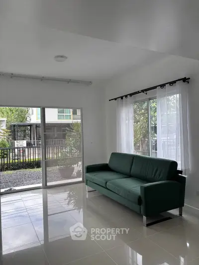 Spacious living room with modern green sofa and large windows overlooking garden.