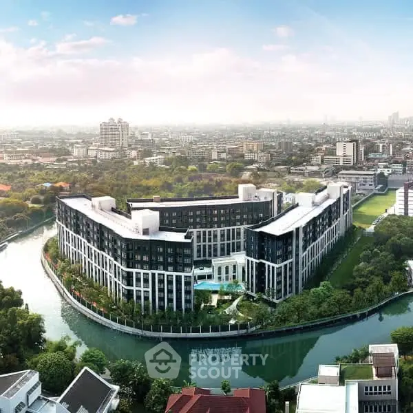 Stunning aerial view of modern riverside apartment complex with lush greenery and cityscape backdrop.
