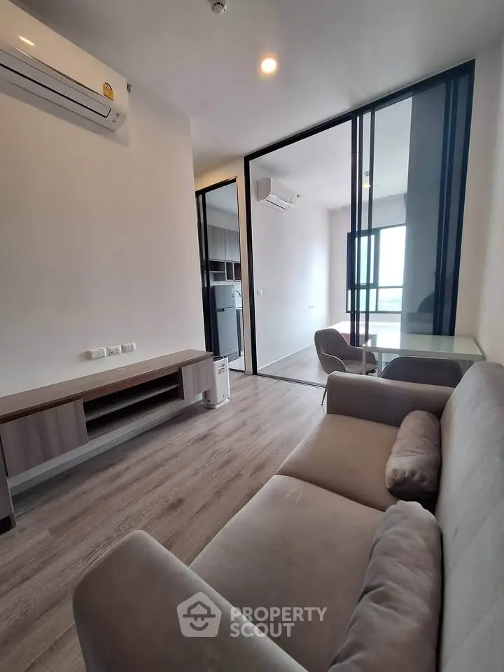 Modern living room with sleek design and glass partition leading to a bright room.