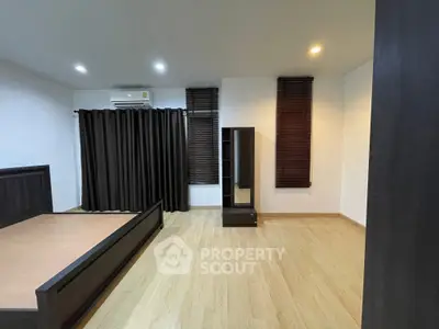 Spacious bedroom with modern wooden flooring and dark curtains