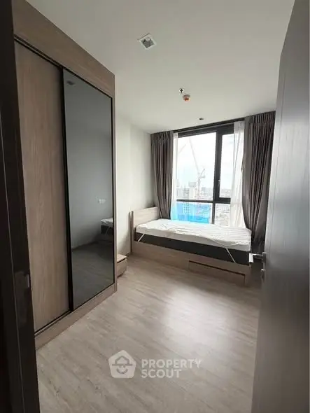 Modern bedroom with large window and wooden flooring, featuring a sleek wardrobe and cozy bed.