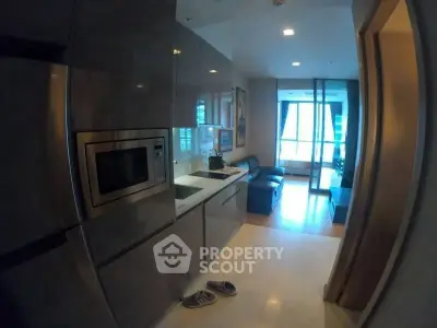 Modern kitchen with sleek cabinetry and integrated appliances leading to a cozy living area.