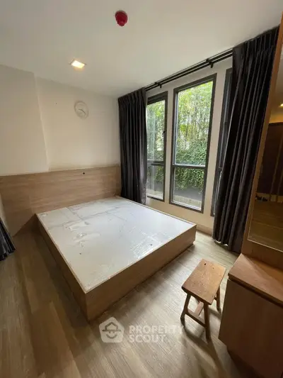 Spacious bedroom with large windows and wooden flooring, offering a serene garden view.