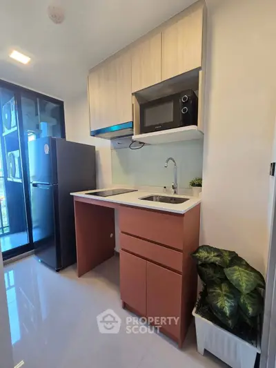 Modern compact kitchen with sleek cabinetry and appliances, featuring a fridge and microwave, ideal for urban living.