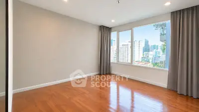 Spacious empty room with large window offering stunning city views and elegant hardwood flooring.