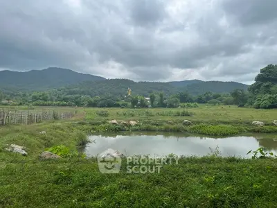 Scenic view of lush green landscape with pond and mountains under cloudy sky