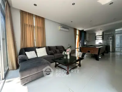 Spacious modern living room with sectional sofa and pool table, open kitchen layout, and abundant natural light.