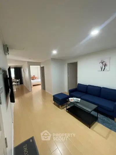 Spacious living room with modern blue sofa and wooden flooring, leading to a cozy bedroom.