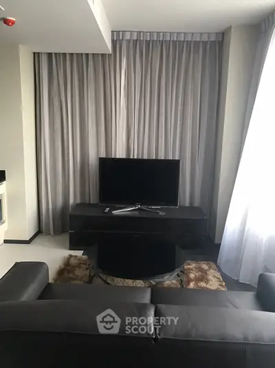 Modern living room with sleek black furniture and large TV, elegant curtains enhance the ambiance.