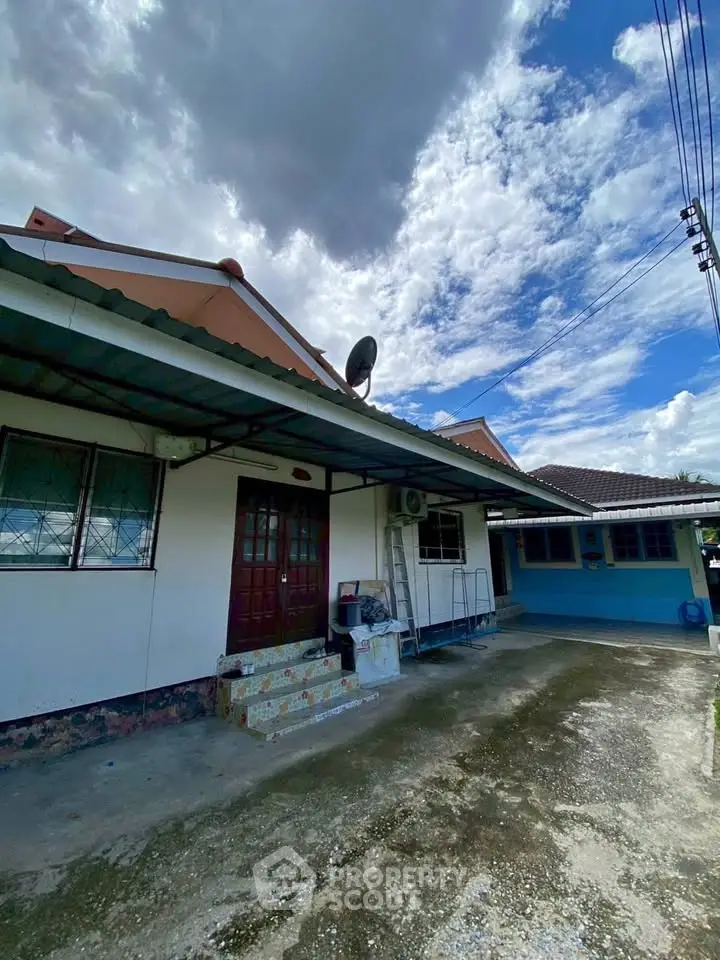 Charming single-story home with spacious driveway and covered entrance under a cloudy sky.