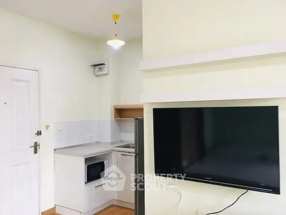 Modern compact kitchen with integrated appliances and wall-mounted TV in cozy apartment.