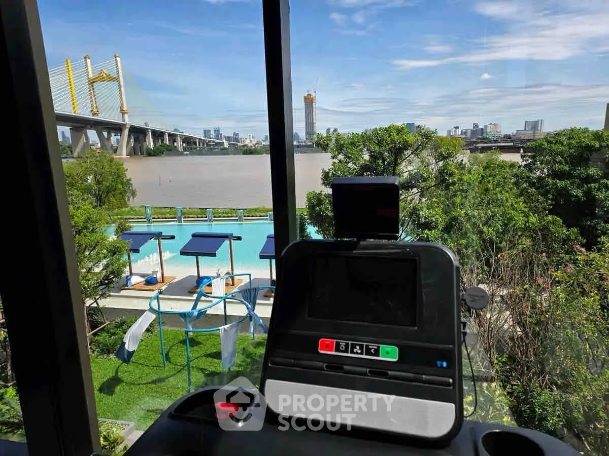 Stunning river view from gym with pool and lush greenery, perfect for fitness enthusiasts.