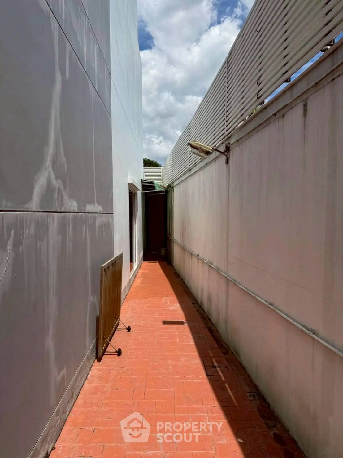 Narrow outdoor corridor with red brick flooring and high walls under a clear sky.
