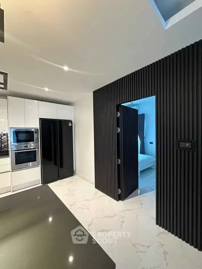 Modern kitchen with sleek black and white design, featuring built-in appliances and marble flooring.