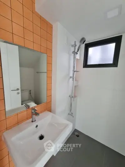 Modern bathroom with orange tiles and sleek fixtures, featuring a shower and sink.