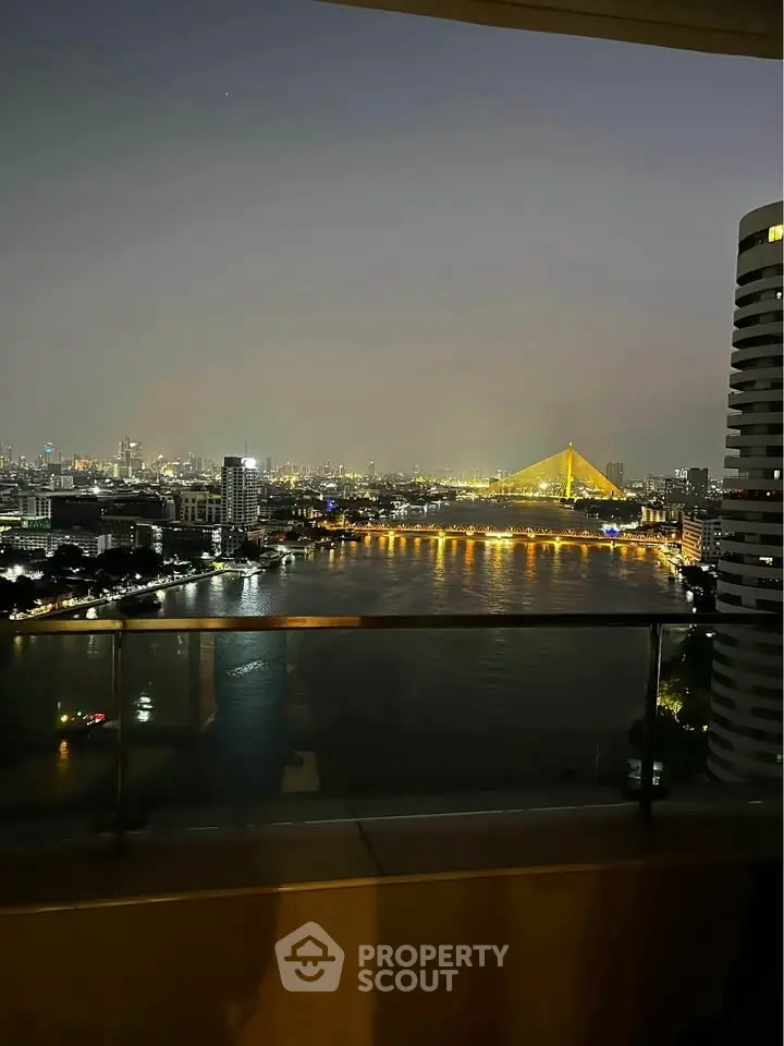 Stunning night view from a high-rise balcony overlooking a river and illuminated cityscape.
