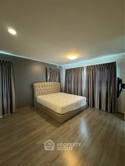 Spacious bedroom with elegant curtains and modern lighting, featuring a stylish bed and wooden flooring.