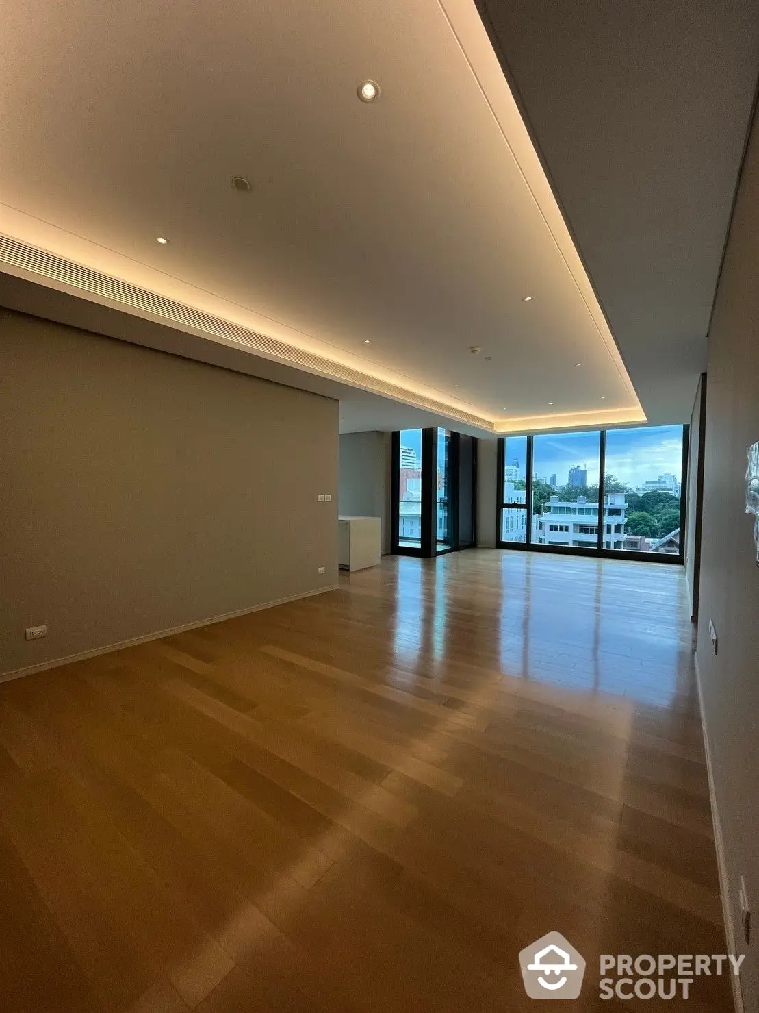 Spacious and modern living room with polished hardwood floors and ample natural light, featuring a sleek design and a panoramic view through floor-to-ceiling windows.