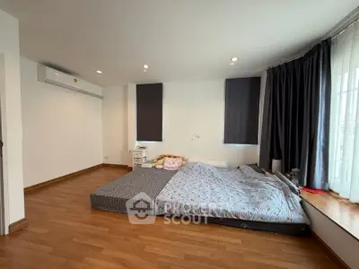 Spacious bedroom with large windows and wooden flooring, featuring a cozy bed setup.