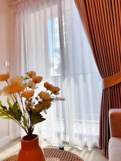 Charming living room with elegant curtains and natural light, featuring a stylish vase with flowers.