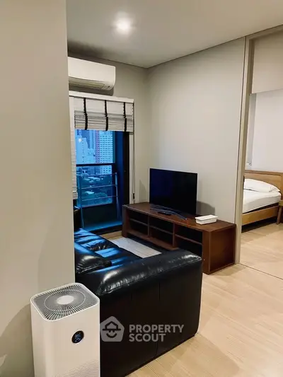Modern living room with sleek black leather sofa and flat-screen TV, featuring a city view from the window.