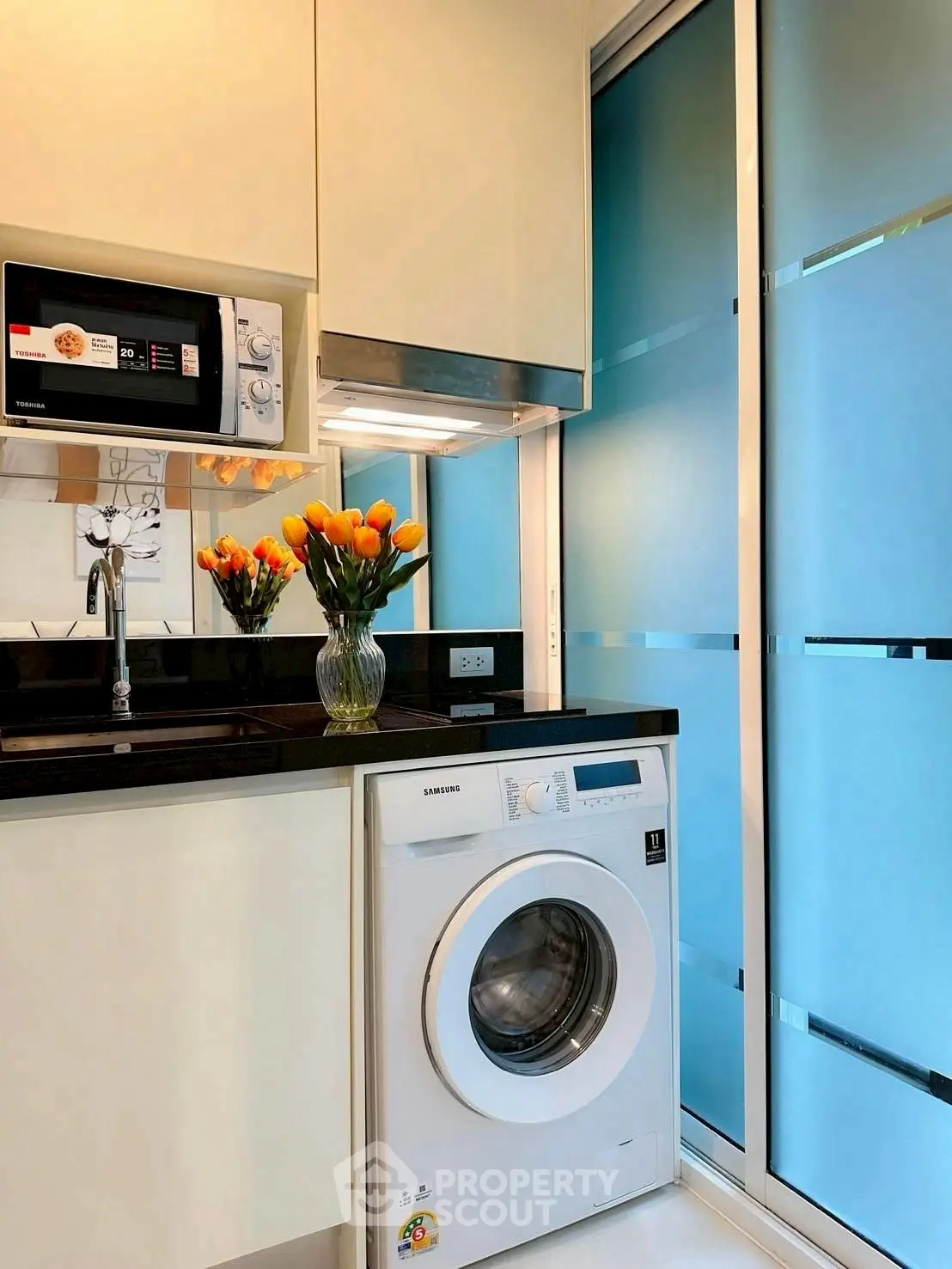 Modern kitchen with sleek appliances and vibrant decor, featuring a washing machine and microwave.