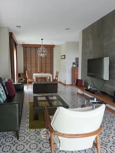 Elegant living room with modern decor and stylish furniture, featuring a wall-mounted TV and chandelier.