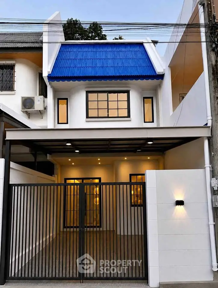 Charming two-story house with blue roof and modern gated entrance, perfect for urban living.