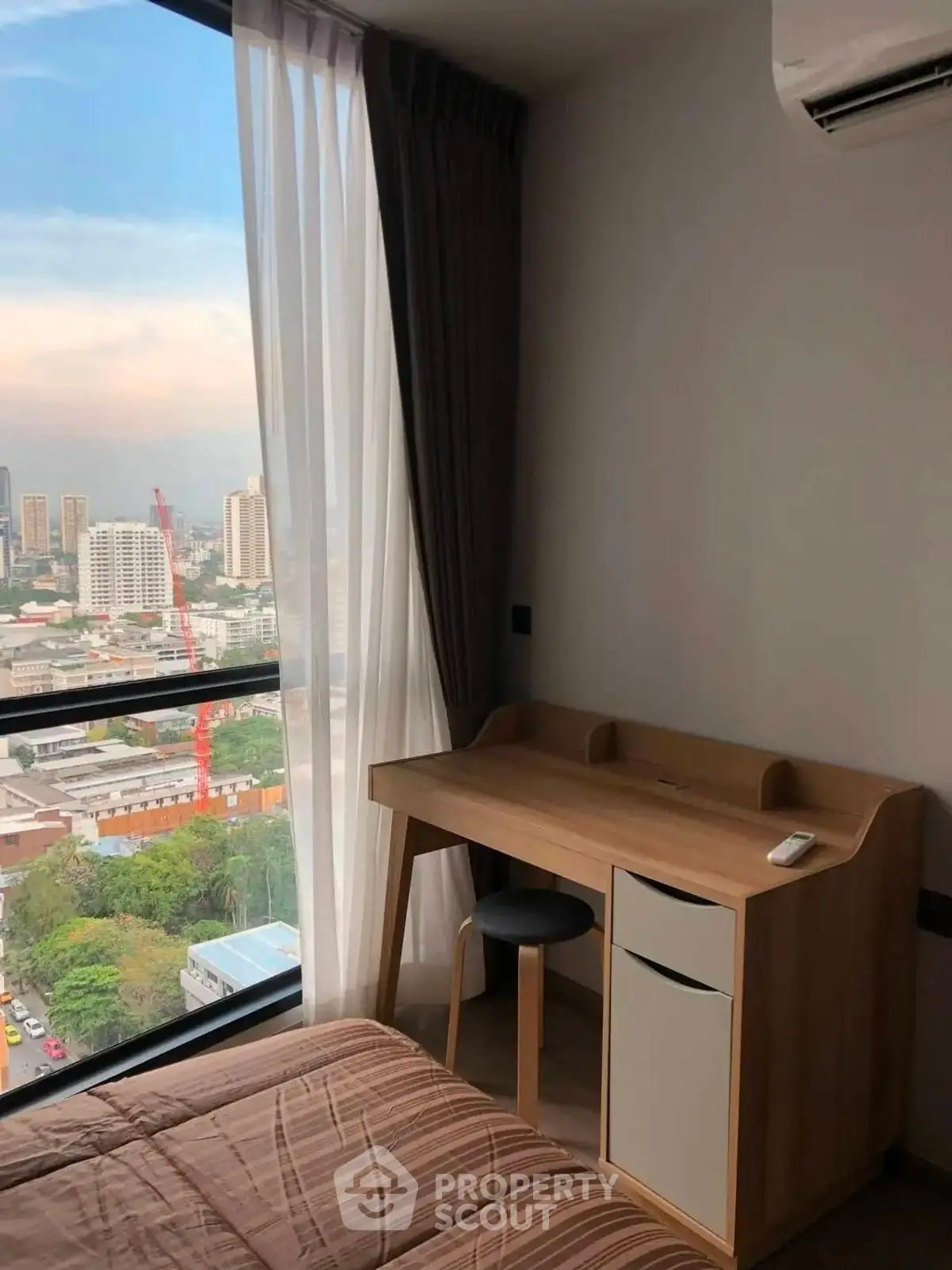 Modern bedroom with city view, featuring a sleek wooden desk and large window.