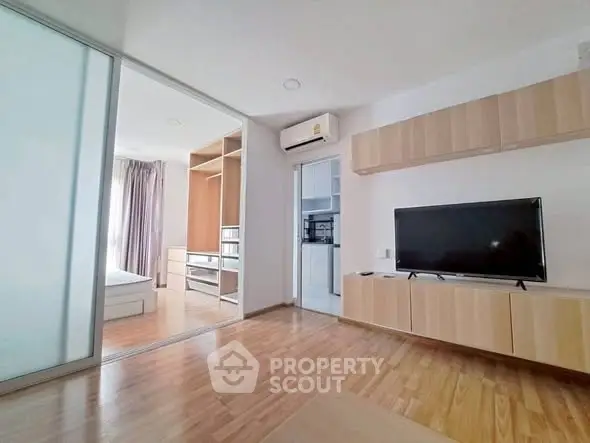 Modern living room with wooden flooring, TV, and sliding doors leading to a bedroom in a stylish apartment.
