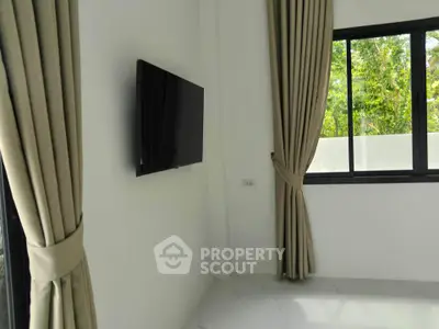 Modern living room with wall-mounted TV and large window with elegant curtains.