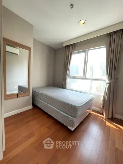 Bright and cozy bedroom with wooden flooring and large window in modern apartment.