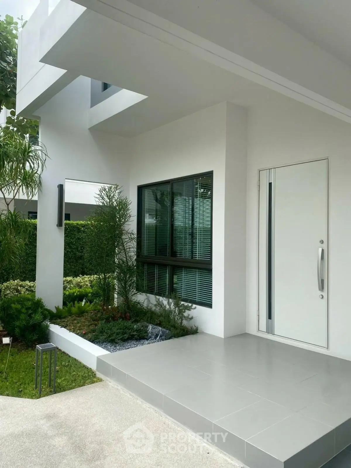 Modern white house entrance with sleek design and lush greenery