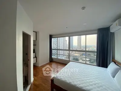 Spacious bedroom with city view and wooden flooring in modern apartment.