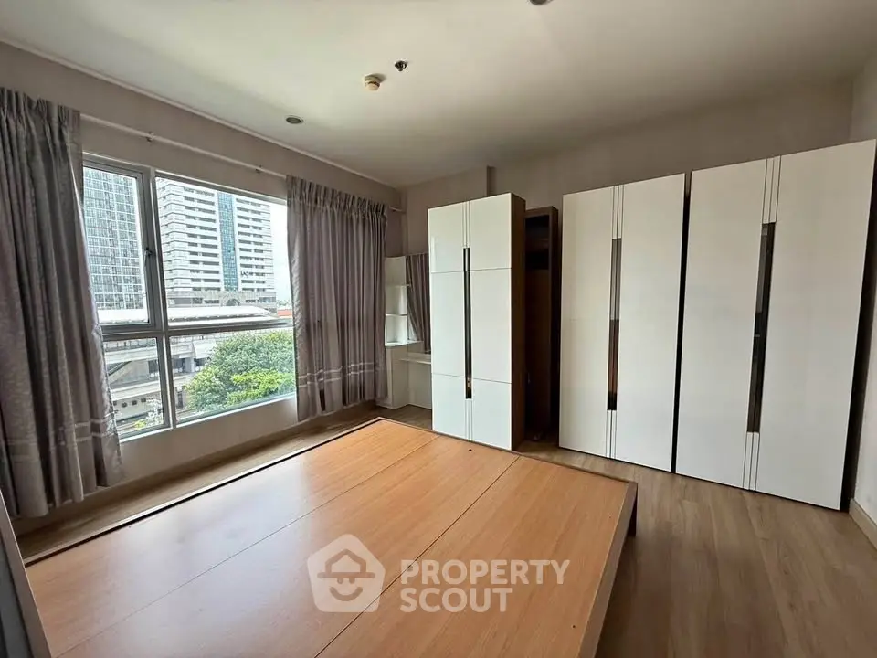 Spacious bedroom with large windows and modern wardrobes in urban apartment.