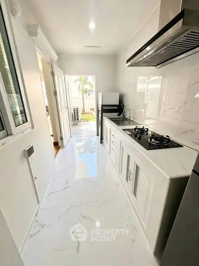 Modern kitchen with sleek design, gas stove, and marble flooring in a bright, airy space.