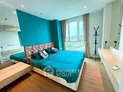 Spacious bedroom with vibrant teal accent wall and city view window.