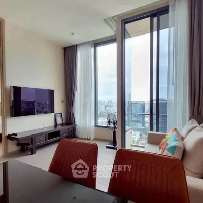 Modern living room with floor-to-ceiling windows offering stunning city views, stylish furniture, and a wall-mounted TV.