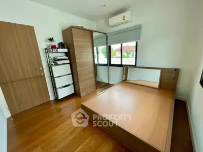 Spacious bedroom with wooden flooring and modern furniture, featuring a large wardrobe and air conditioning.