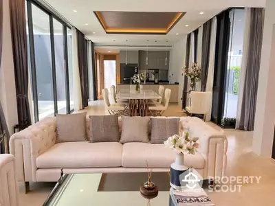 Luxurious open-plan living space with elegant cream sofa set, sleek dining area, and modern kitchen, bathed in natural light from floor-to-ceiling windows, perfect for entertaining.