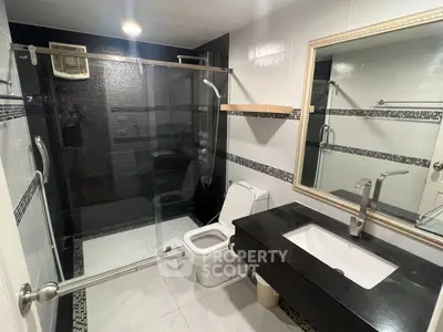 Modern bathroom with sleek black and white design, glass shower enclosure, and elegant fixtures.